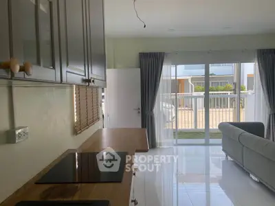 Modern kitchen with sleek cabinetry and open layout leading to a bright living area with large windows.