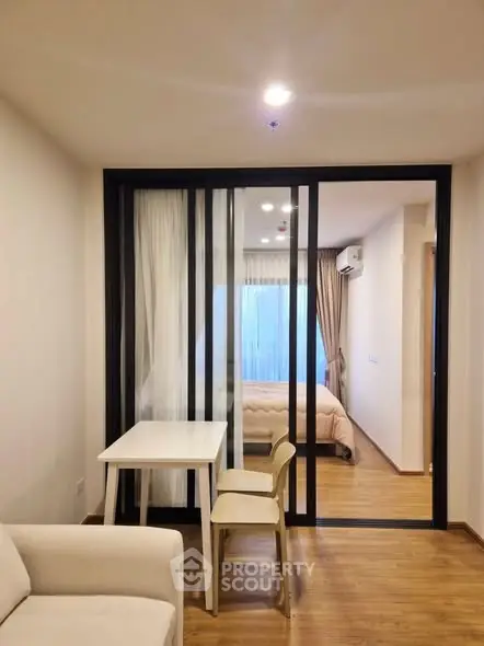 Modern apartment interior with sliding glass doors separating living and bedroom areas, featuring wooden flooring.