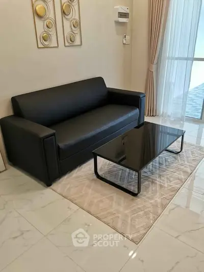 Modern living room with sleek black sofa and glass coffee table on elegant rug.