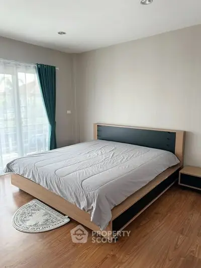 Spacious bedroom with modern wooden flooring and large window for natural light.