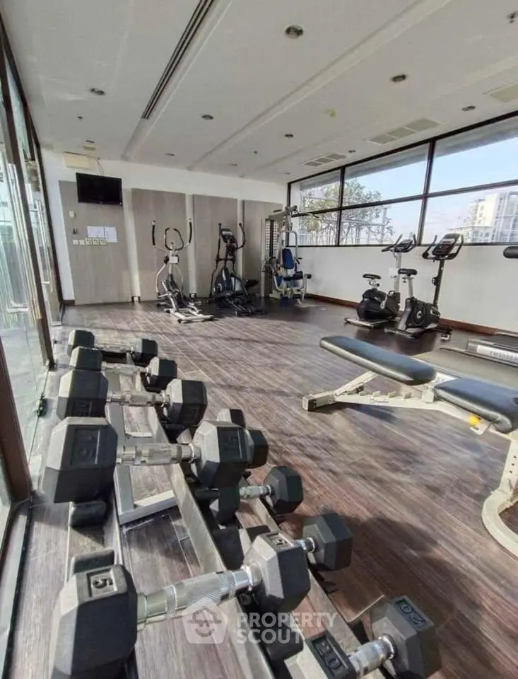 Spacious gym with modern equipment and large windows offering city views, perfect for fitness enthusiasts.