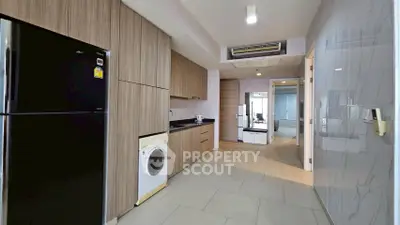 Modern kitchen with sleek wooden cabinets, black fridge, and washing machine in a spacious apartment.