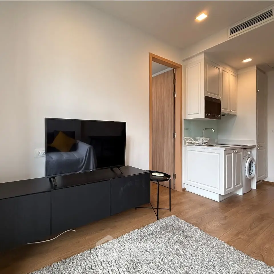 Modern living room with sleek TV unit and compact kitchen featuring washing machine.