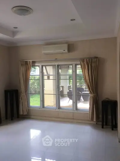 Spacious living room with large window and garden view, featuring elegant curtains and air conditioning.