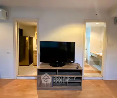 Cozy living room with TV stand, adjacent kitchen and bathroom entryways.