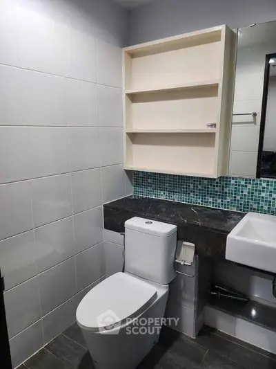 Modern bathroom with sleek toilet, wall-mounted shelves, and stylish tile backsplash.