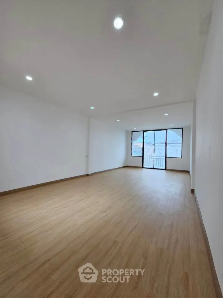 Spacious empty room with wooden flooring and large windows, ideal for customization.
