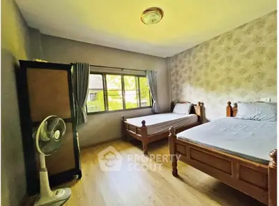 Cozy bedroom with twin beds and a fan, featuring a large window and wooden flooring.