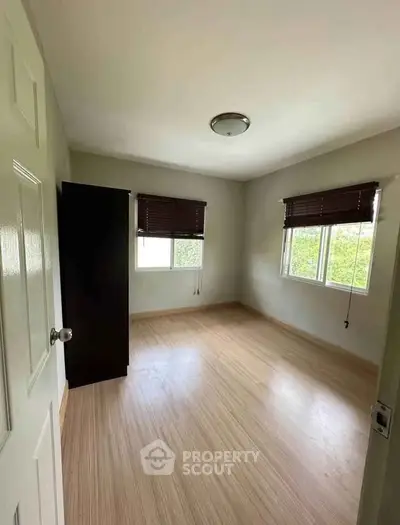 Spacious empty bedroom with wooden flooring and natural light from two windows.