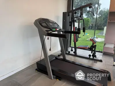 Modern home gym with treadmill and multi-exercise machine overlooking garden view.