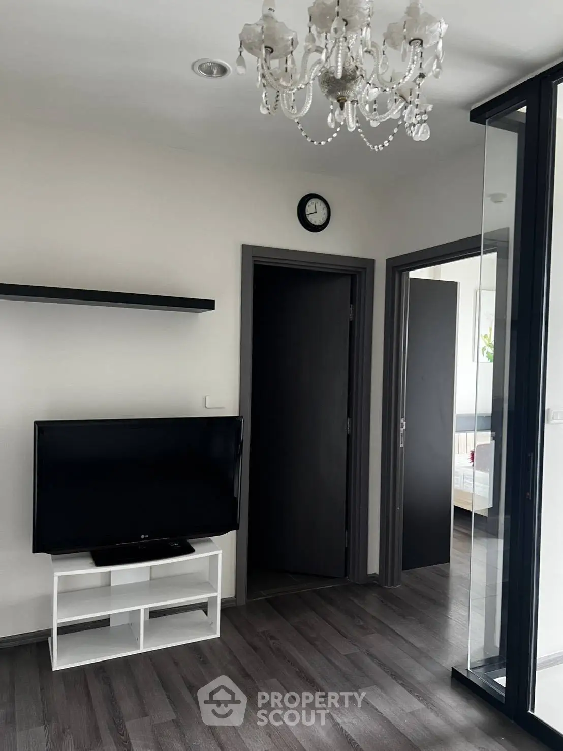 Modern living room with chandelier and TV, featuring sleek flooring and minimalist decor.