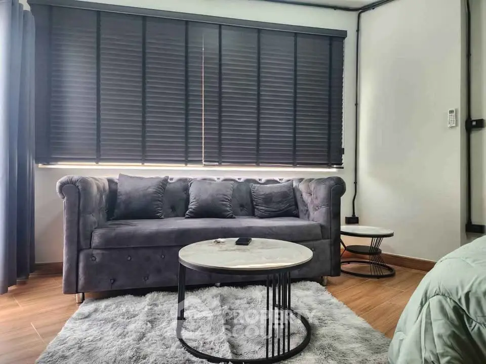 Modern living room with stylish sofa and coffee table, featuring elegant blinds and cozy rug.