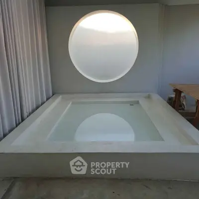 Modern minimalist bathroom with unique circular window and built-in bathtub.