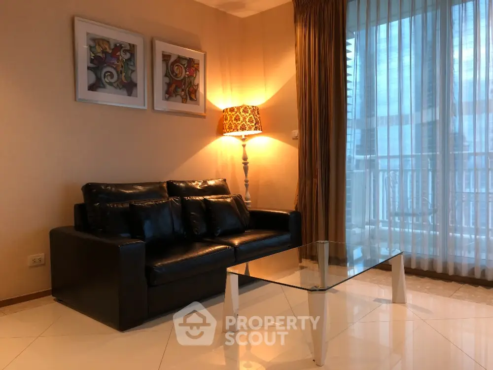 Elegant living room with leather sofa and glass coffee table, featuring modern art and warm lighting.
