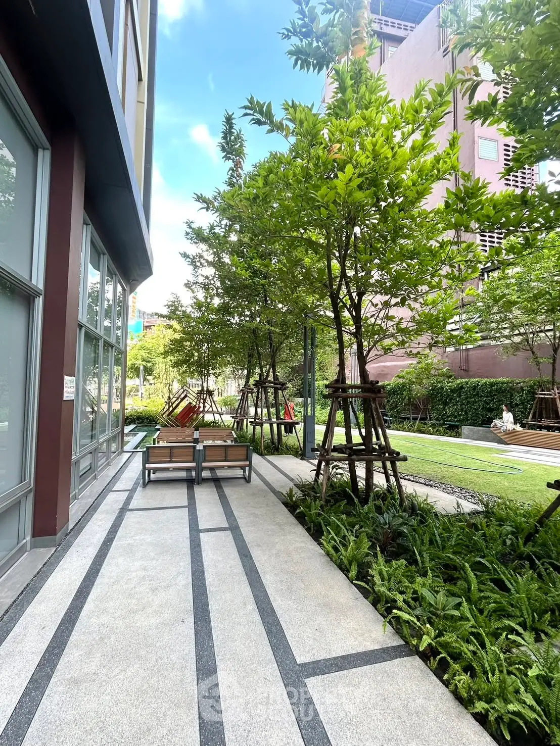 Modern apartment building exterior with lush garden and seating area, perfect for relaxation.