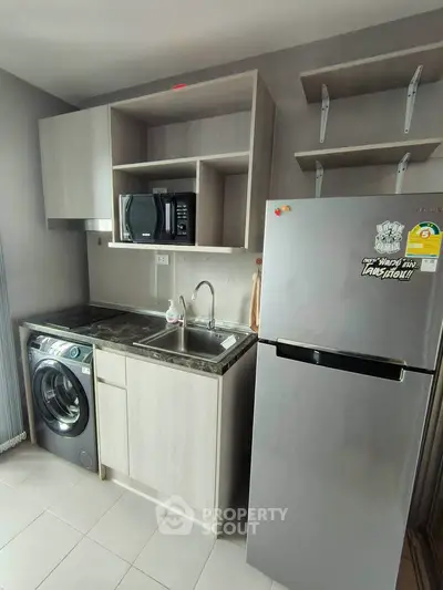 Modern kitchen with washing machine, microwave, and fridge in compact layout.