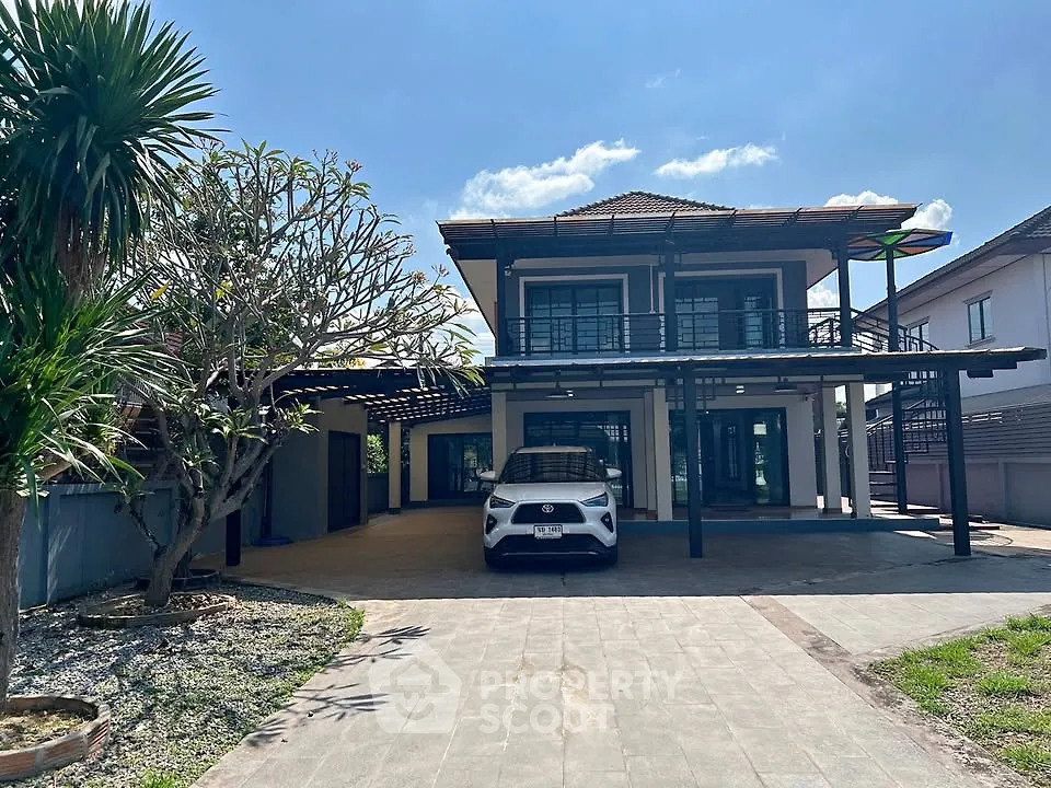 Modern two-story house with spacious driveway and carport, surrounded by lush greenery and clear blue sky.