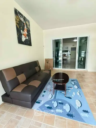 Spacious living room with modern sofa and artistic decor, leading to a bright kitchen area.