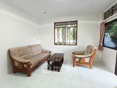Cozy living room with wooden furniture and natural light through large windows.