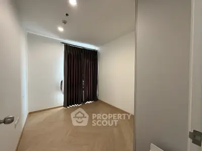 Spacious empty room with elegant wooden flooring and large window with dark curtains.