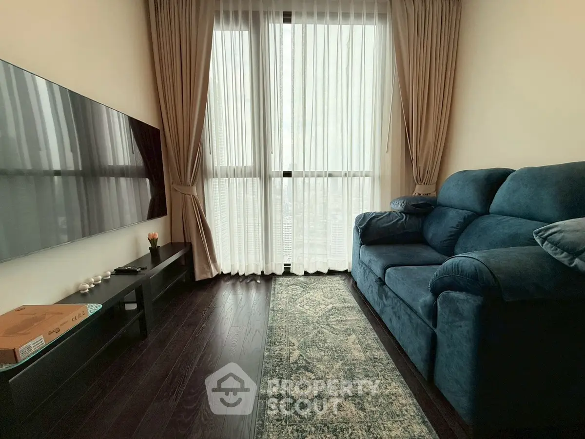 Cozy living room with plush blue sofa and large TV, featuring floor-to-ceiling windows and elegant curtains.