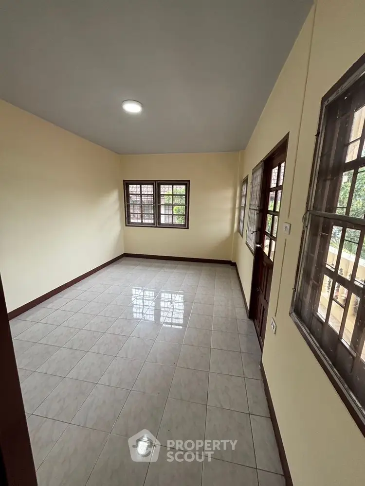 Spacious empty room with tiled flooring and large windows offering natural light.