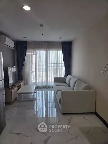 Modern living room with sleek white sofa and large windows offering natural light.