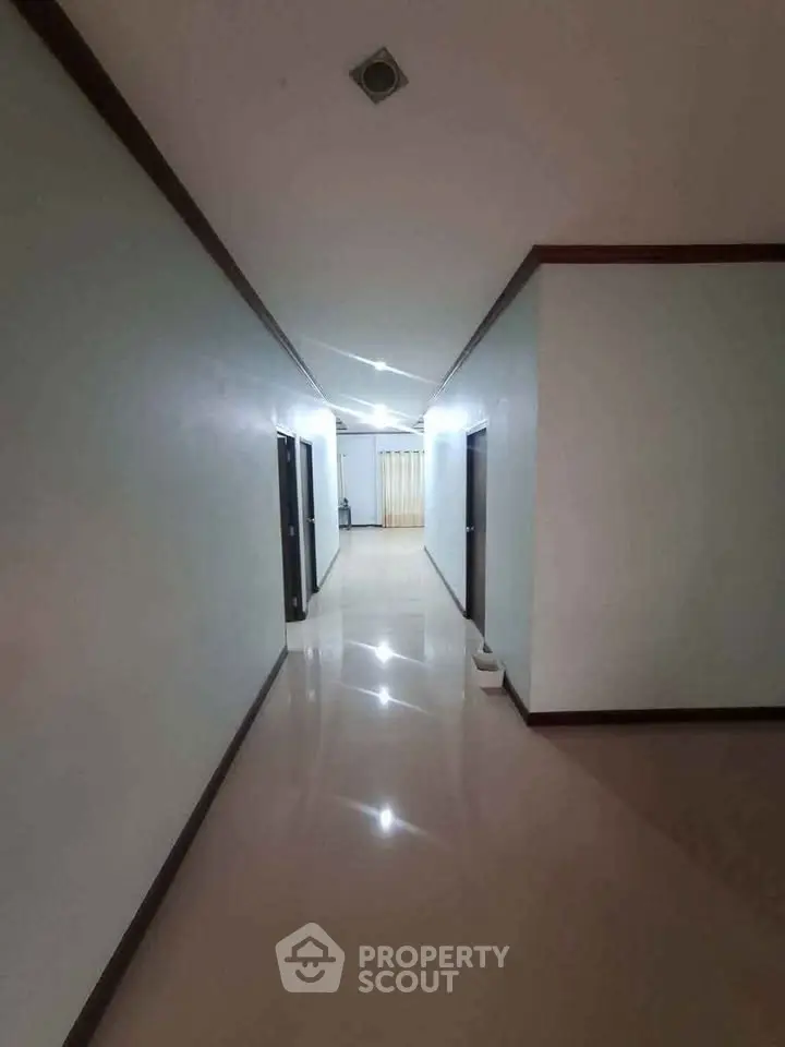 Spacious corridor with polished floors and modern lighting in a residential building.