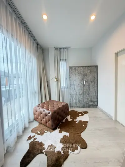 Stylish modern room with large windows, chic ottoman, and cowhide rug, perfect for a cozy living space.