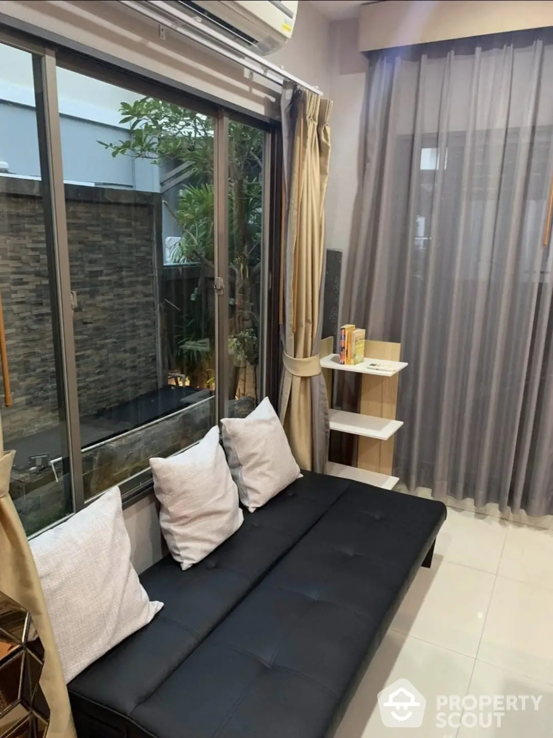 Cozy living space with sleek black sofa, elegant drapery, and a view of a serene private garden through floor-to-ceiling glass doors, perfect for relaxation.