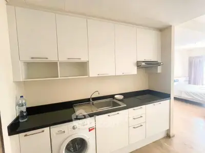 Modern kitchen with sleek white cabinets and built-in washing machine in a bright apartment.