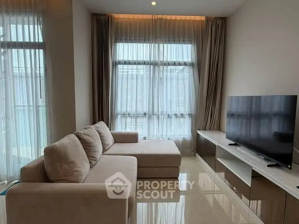 Modern living room with large windows, elegant curtains, and a cozy beige sofa facing a sleek TV unit.