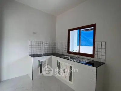 Modern kitchen with sleek black countertops and white tiled backsplash, featuring a large window for natural light.