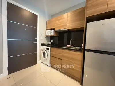 Modern kitchen with wooden cabinets, washing machine, and stainless steel fridge