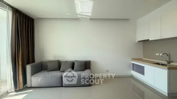 Modern minimalist living room with sleek kitchen and cozy gray sofa.