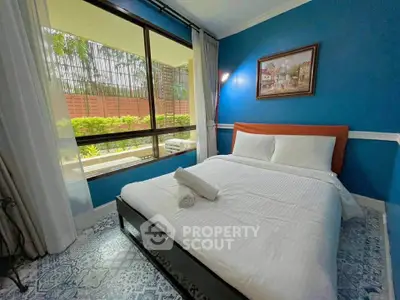 Charming bedroom with blue accent wall and large window overlooking lush greenery.
