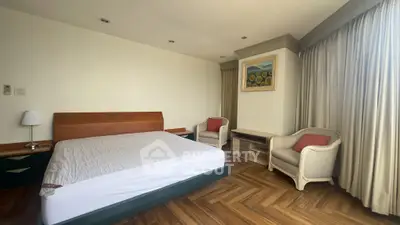 Spacious bedroom with elegant wooden flooring and cozy seating area, perfect for relaxation.