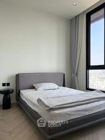 Modern bedroom with city view, featuring a sleek bed and floor-to-ceiling window for natural light.