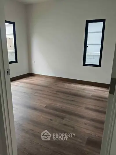 Spacious empty room with wooden flooring and two windows, perfect for customization.