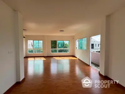 Spacious sunlit living room with large windows and wooden flooring in modern home.