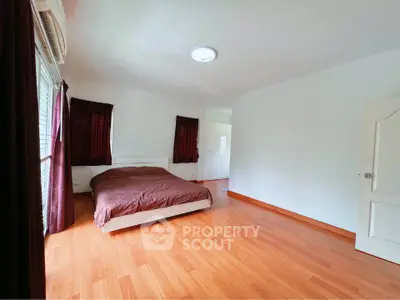 Spacious bedroom with wooden flooring and natural light
