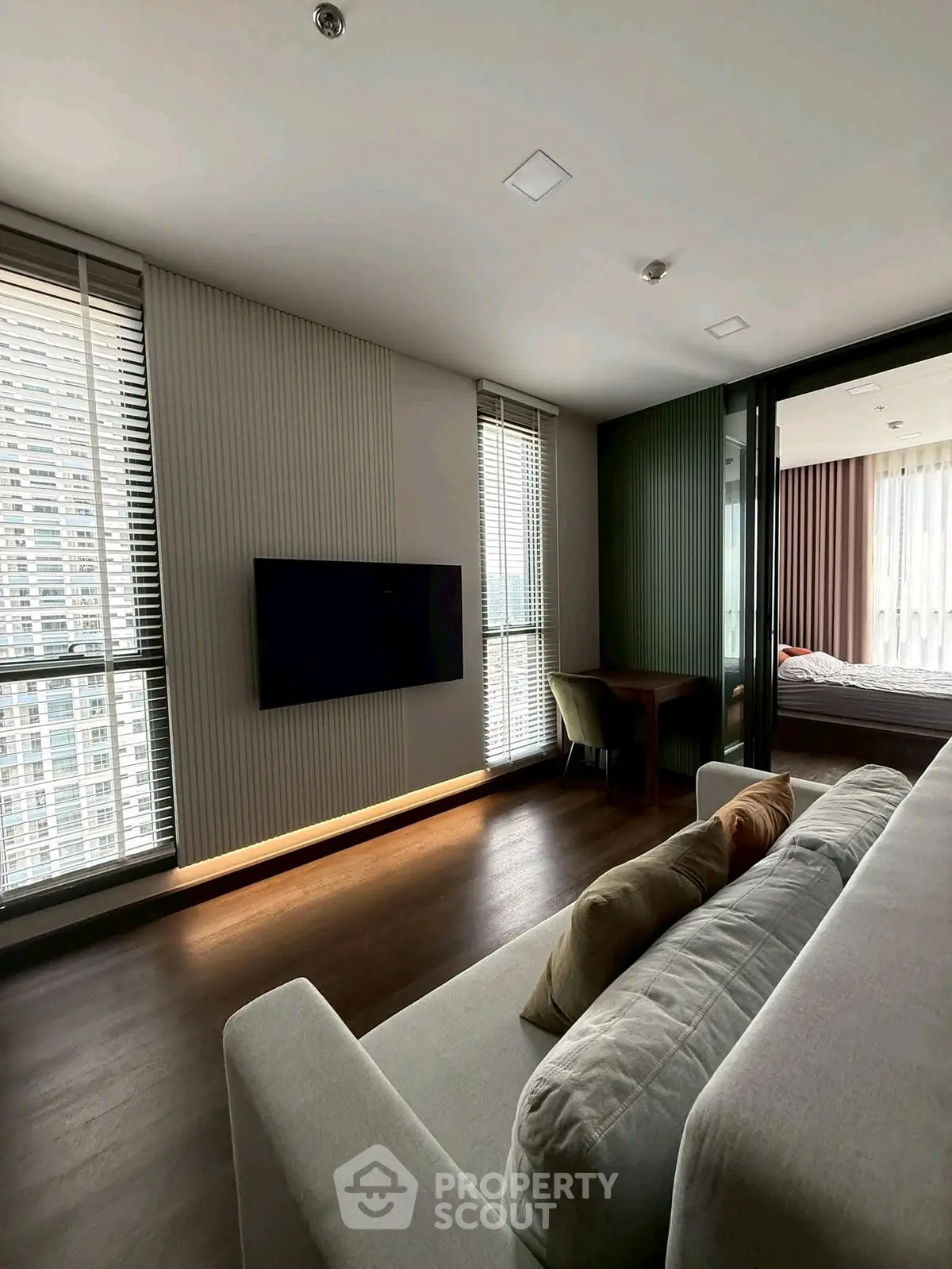 Modern living room with sleek design and large windows offering city views, connected to a cozy bedroom.