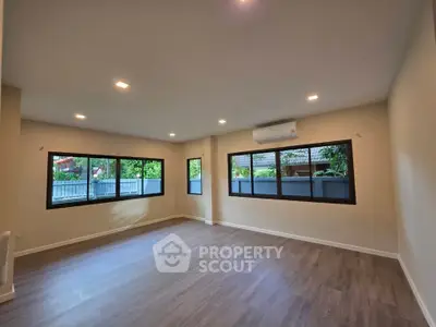 Spacious living room with large windows and modern flooring in a serene setting.