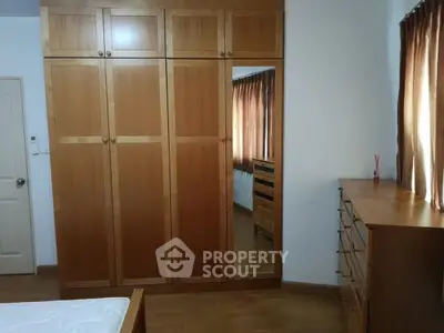 Spacious bedroom with wooden wardrobe and dresser, natural light from window.