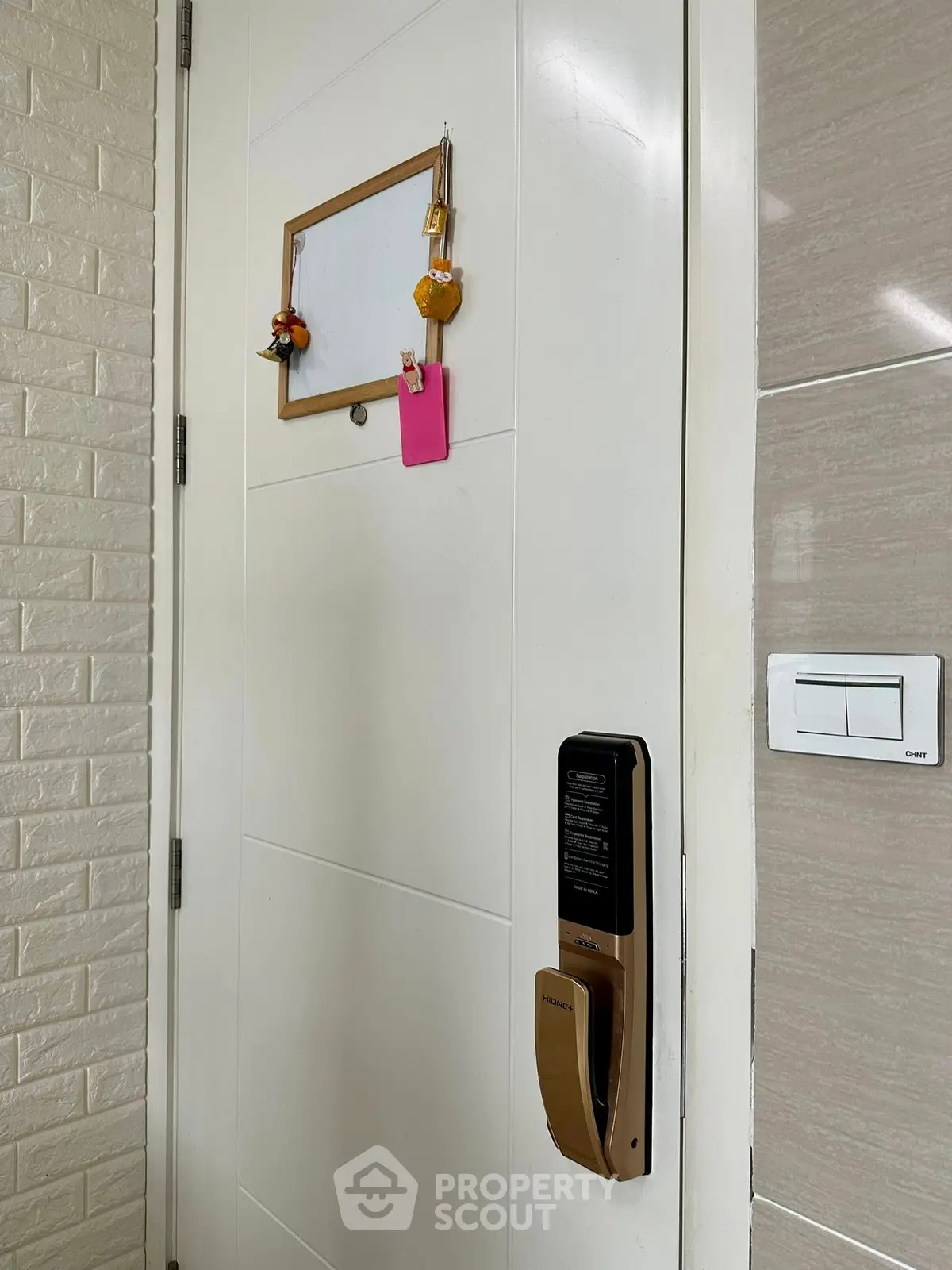 Modern apartment entrance with digital lock and whiteboard for notes.