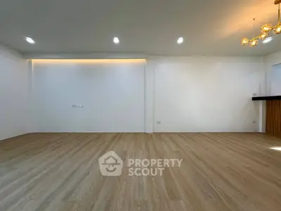 Spacious empty room with wooden flooring and modern lighting, perfect for customization.