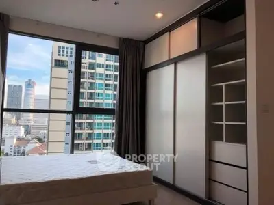 Modern bedroom with city view and built-in wardrobe in high-rise apartment.