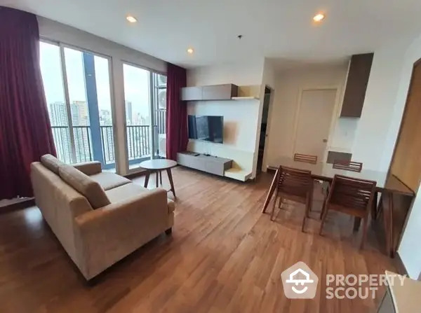 Spacious living room with modern furnishings, hardwood floors, and ample natural light from floor-to-ceiling windows leading to a balcony with a view.