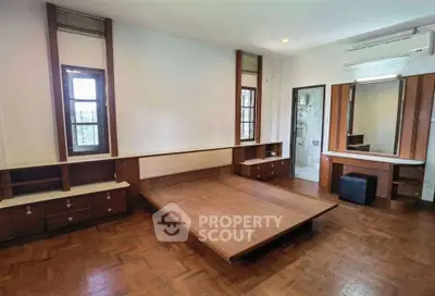 Spacious bedroom with wooden flooring and built-in furniture, featuring large windows and air conditioning.