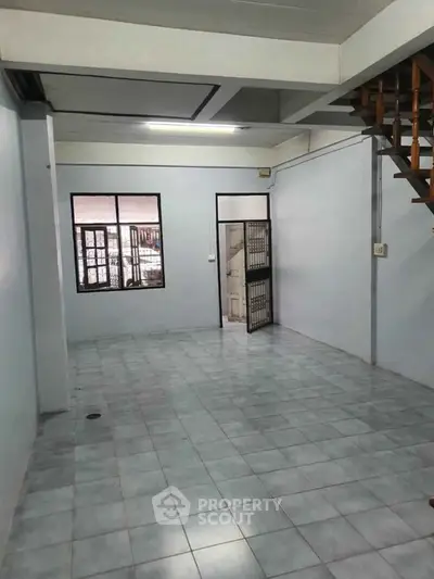 Spacious empty room with tiled flooring and staircase, ideal for customization.
